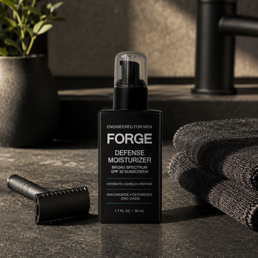 FORGE Defense Moisturizer SPF 30 on a dark stone bathroom counter with a matte black safety razor and a folded charcoal towel in warm morning light