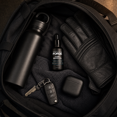 FORGE Core Beard Oil in an open black tactical bag with water bottle, leather gloves, keys and earbuds in warm light